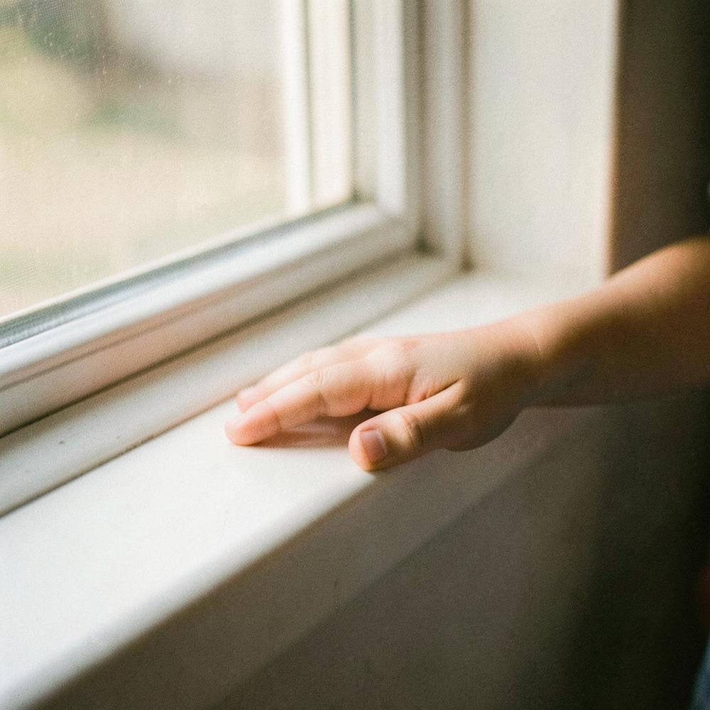 Mão de criança pousada no parapeito de uma janela